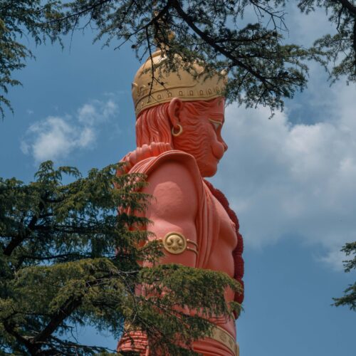 Grand statue of Lord Hanuman surrounded by trees against a blue sky at Jakhoo Temple in Shimla.