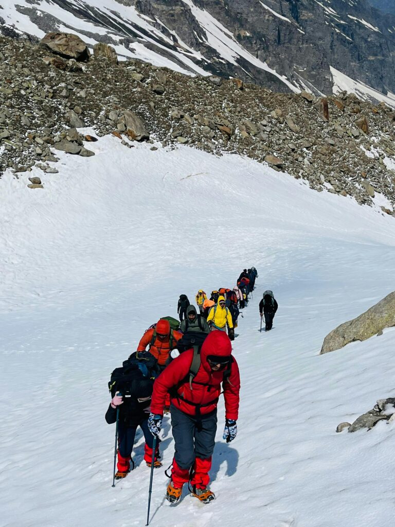 Group of trekkers hiking through snowy terrain in Hampta Pass, India.
