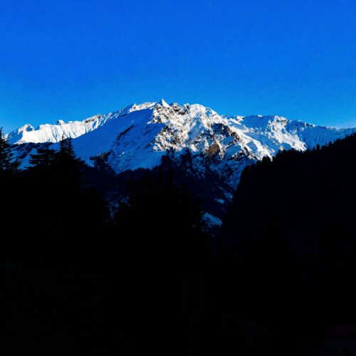 Majestic snowcapped mountains under a vibrant blue sky, captured in Manali, India.