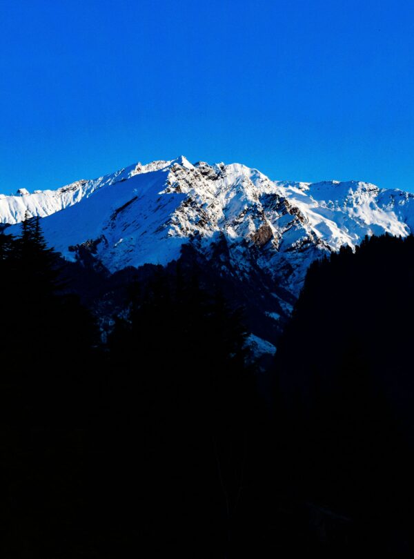 Majestic snowcapped mountains under a vibrant blue sky, captured in Manali, India.
